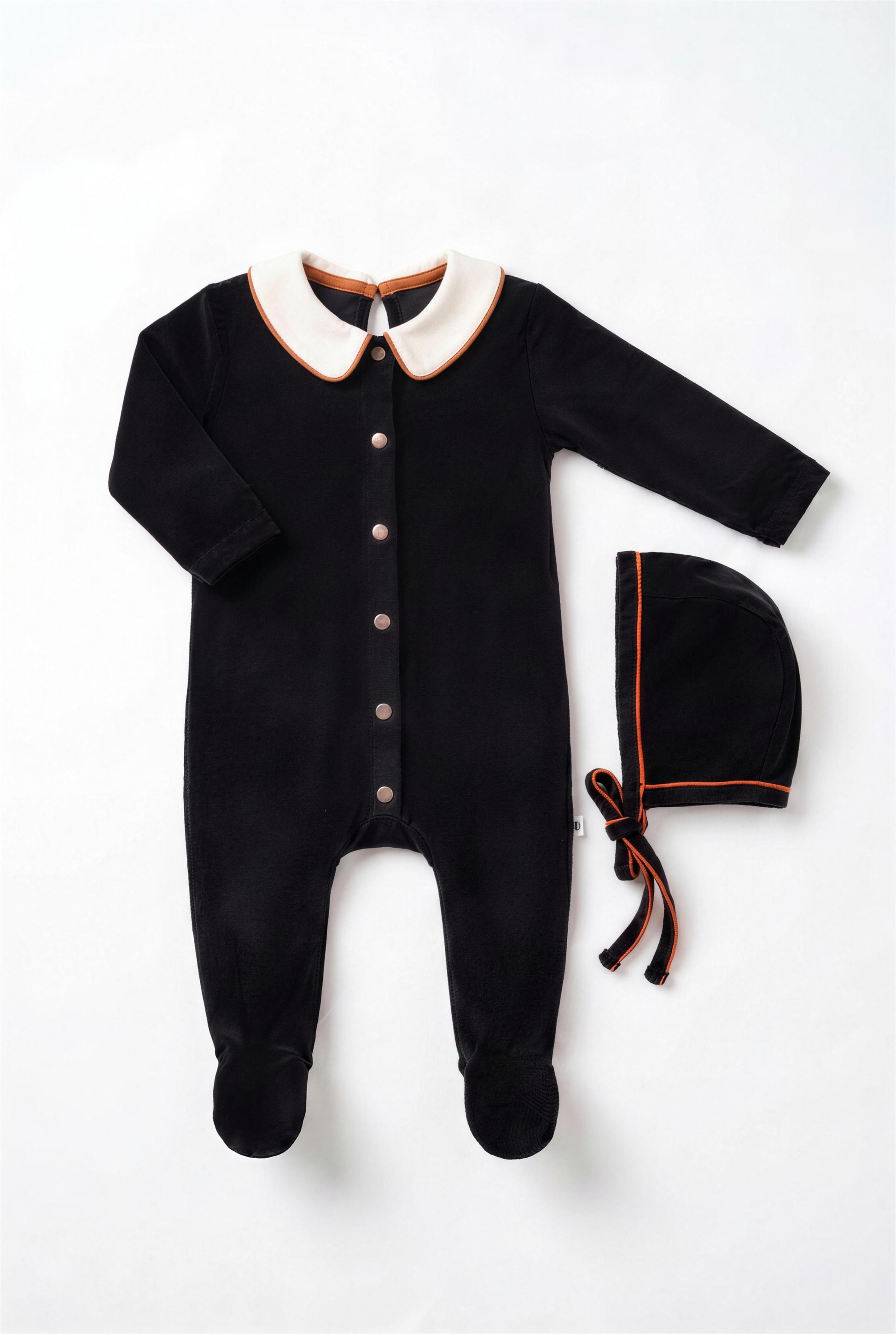 Dottie Lou Classic Noir boys baby footie pajama with matching hat, black velour with ivory collar and orange piping — flatlay