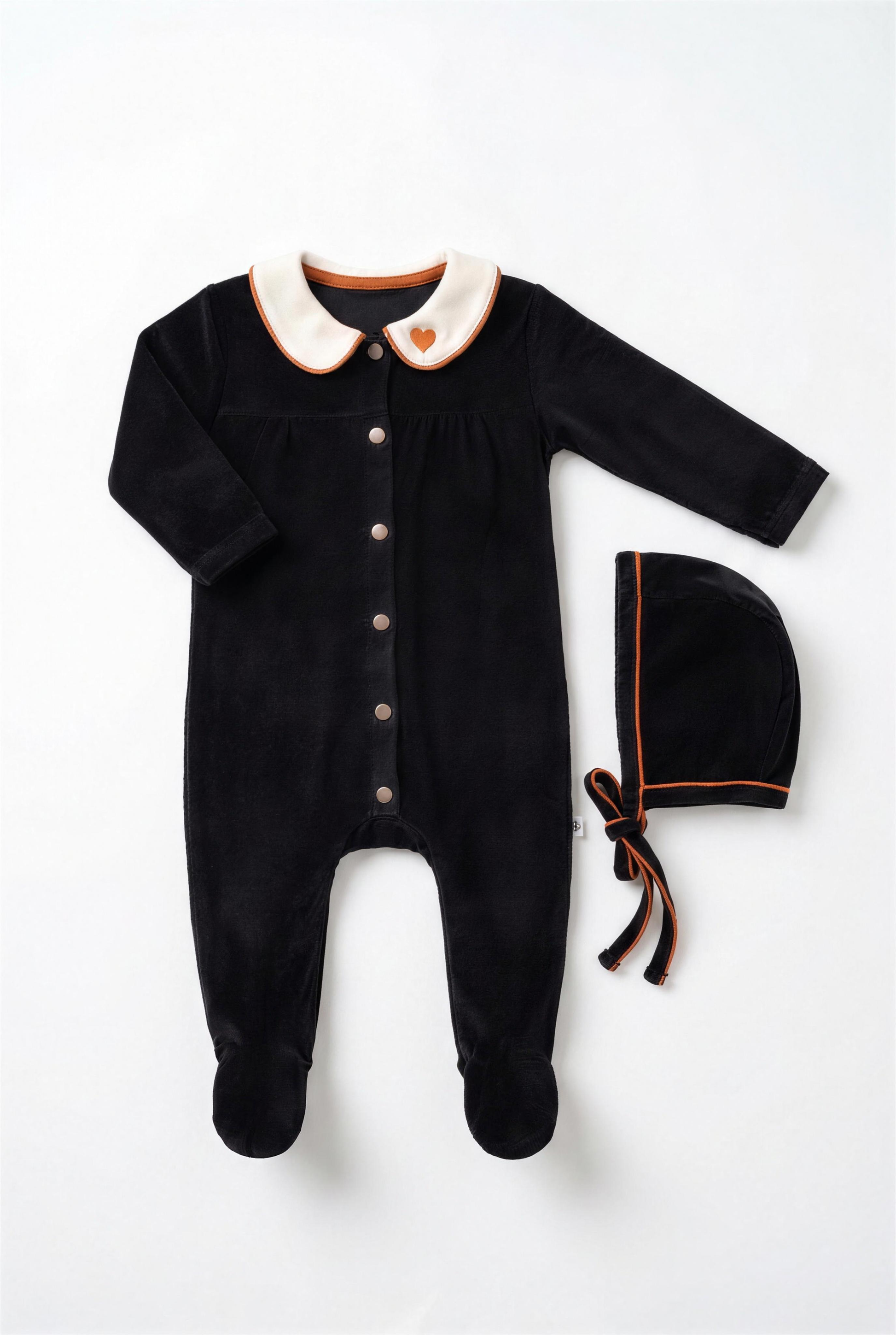 Dottie Lou Classic Noir girls baby footie pajama with matching hat, black velour with ivory collar, orange piping and heart detail — flatlay