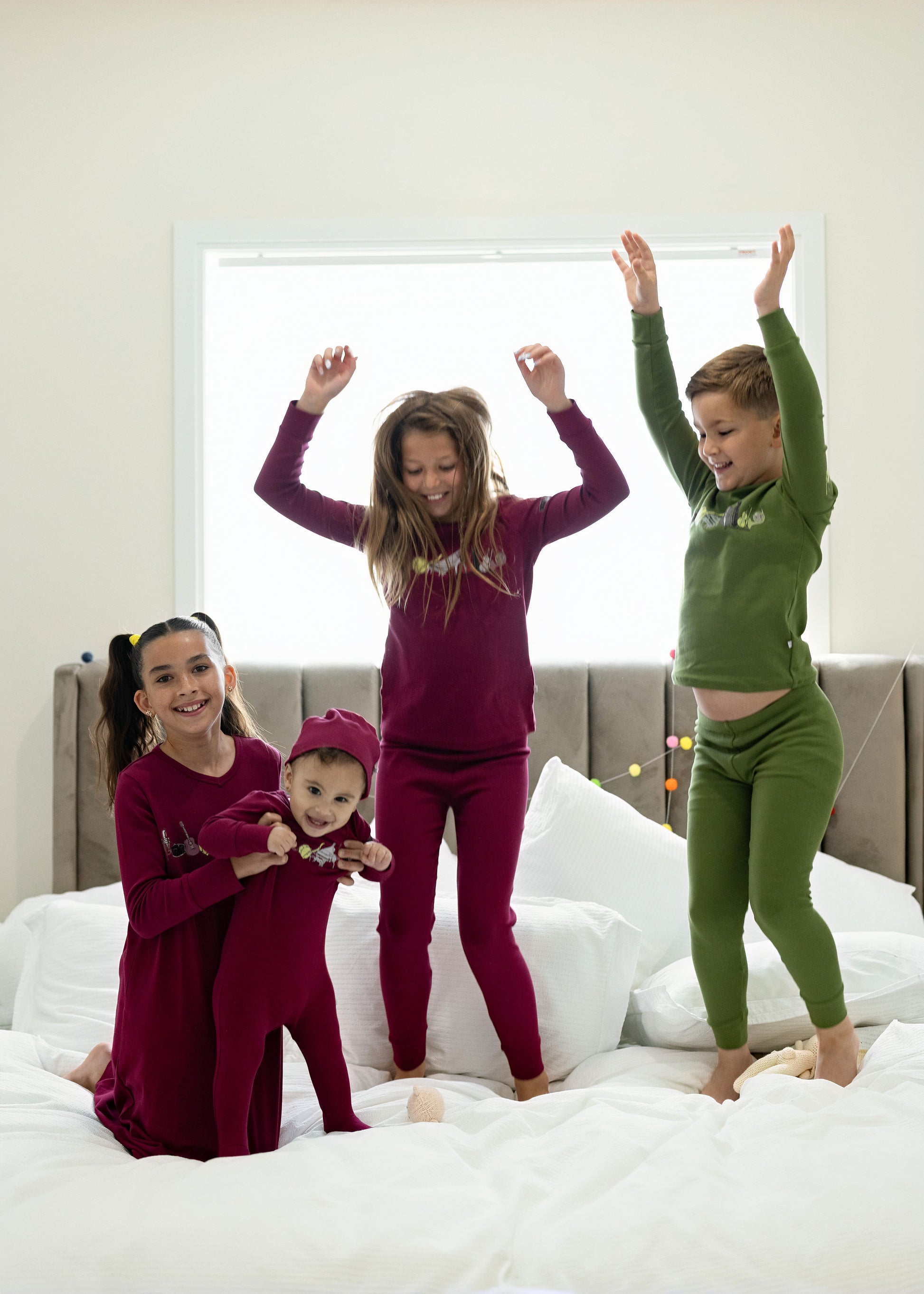 Children in matching Dottie Lou Melody berry and moss green music-print pajamas jumping on a bed