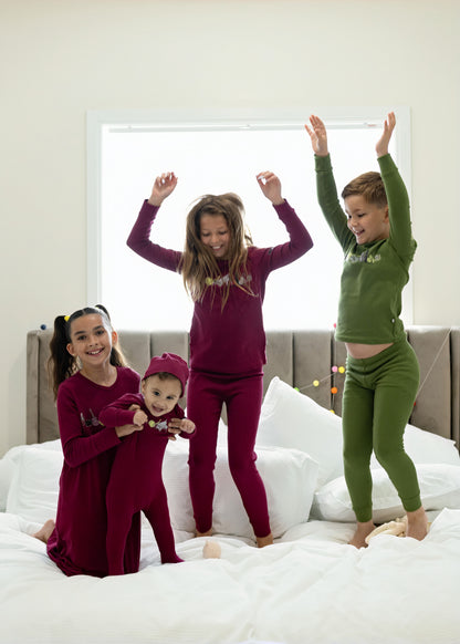 Children in matching Dottie Lou Melody berry and moss green music-print pajamas jumping on a bed